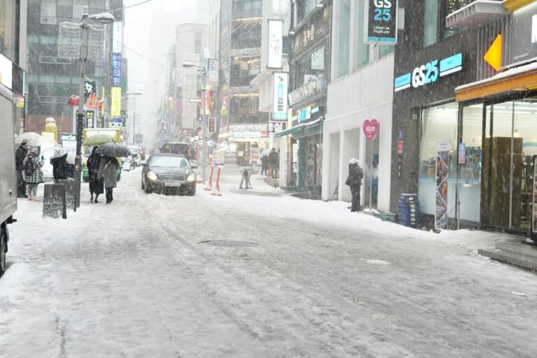 a city street is covered in snow as people walk on the sidewalk